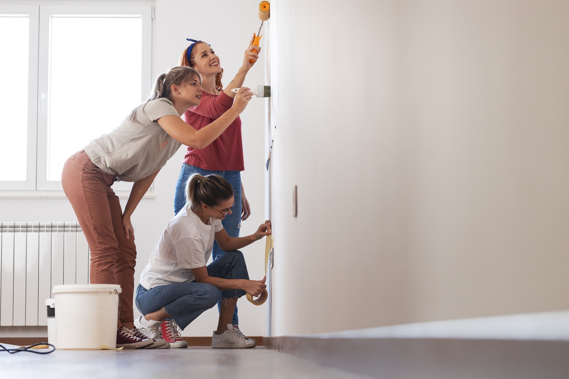 Female roommates using paint roller to decorate the walls in their new home.